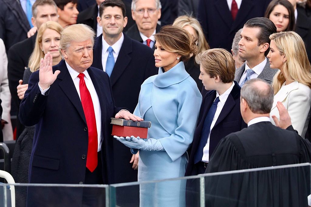 With right hand raised, Donald Trump looks at John Roberts with his back to the camera, as Melania Trump and others watch