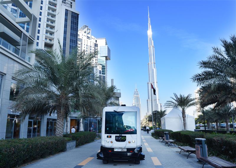 Driverless electric shuttle EZ10 against the backdrop of the towering Burj Khalifa in Dubai. 